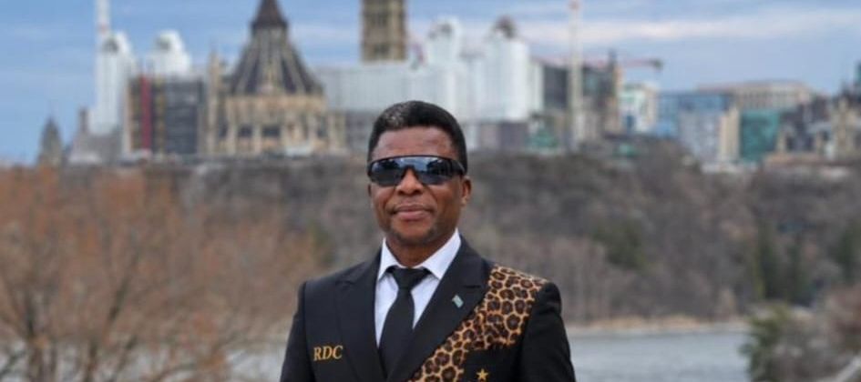 A man in a black suit with leopard braid trim in front of Parliament Hill