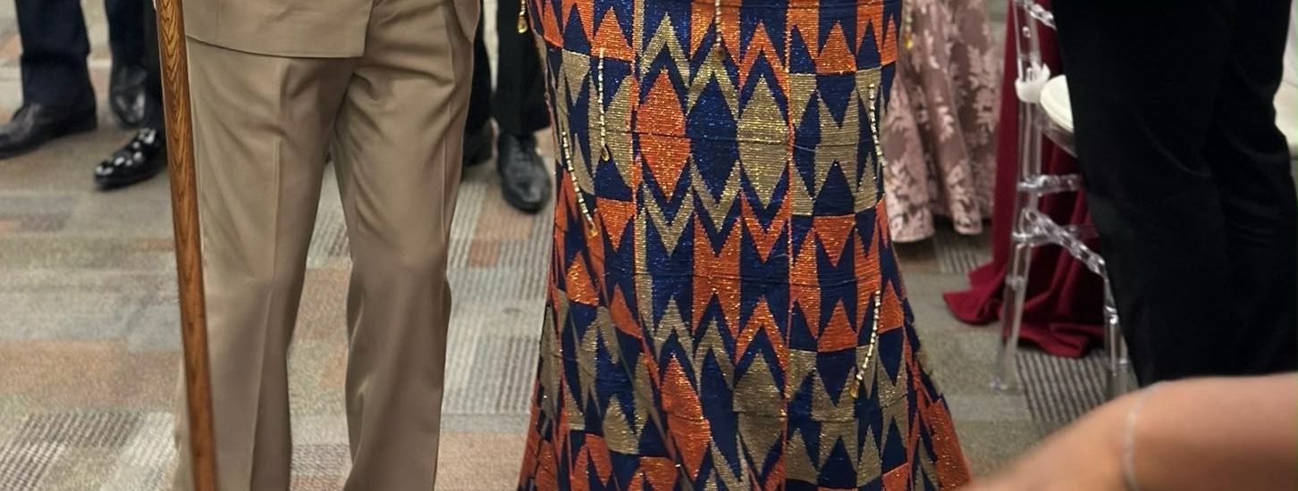 Close-up of a kente gown and a beige outfit at a ceremony