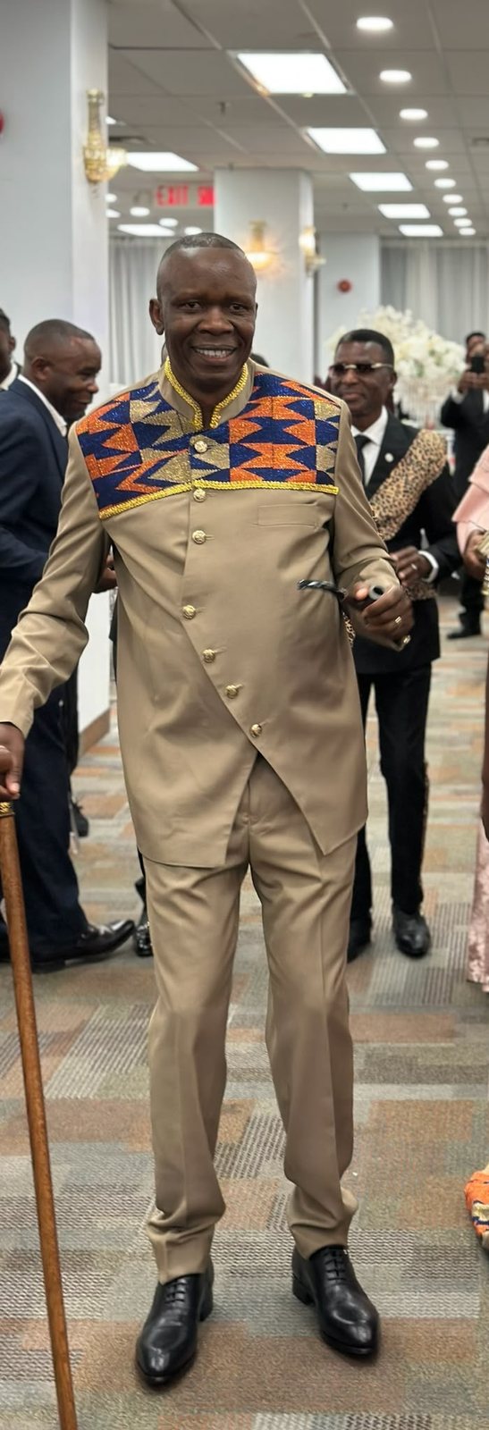 Men's beige outfit with gold buttons and an orange, blue and gold kente bib